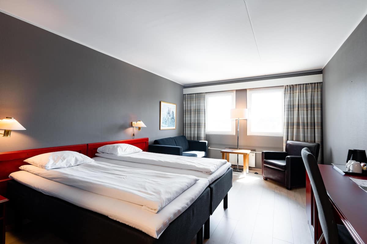 Habitación de hotel con dos camas, un escritorio, una silla, una mesita y una ventana con cortinas.