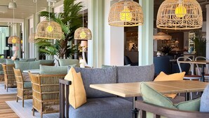A modern restaurant interior with wicker furniture, grey upholstered seating, and hanging wicker lamps. - Havna Hotel & Sjøbad (Færder)