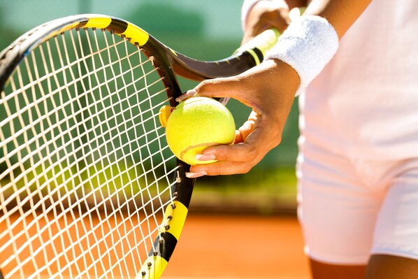 A close-up of a tennis racket and a hand holding a tennis ball.