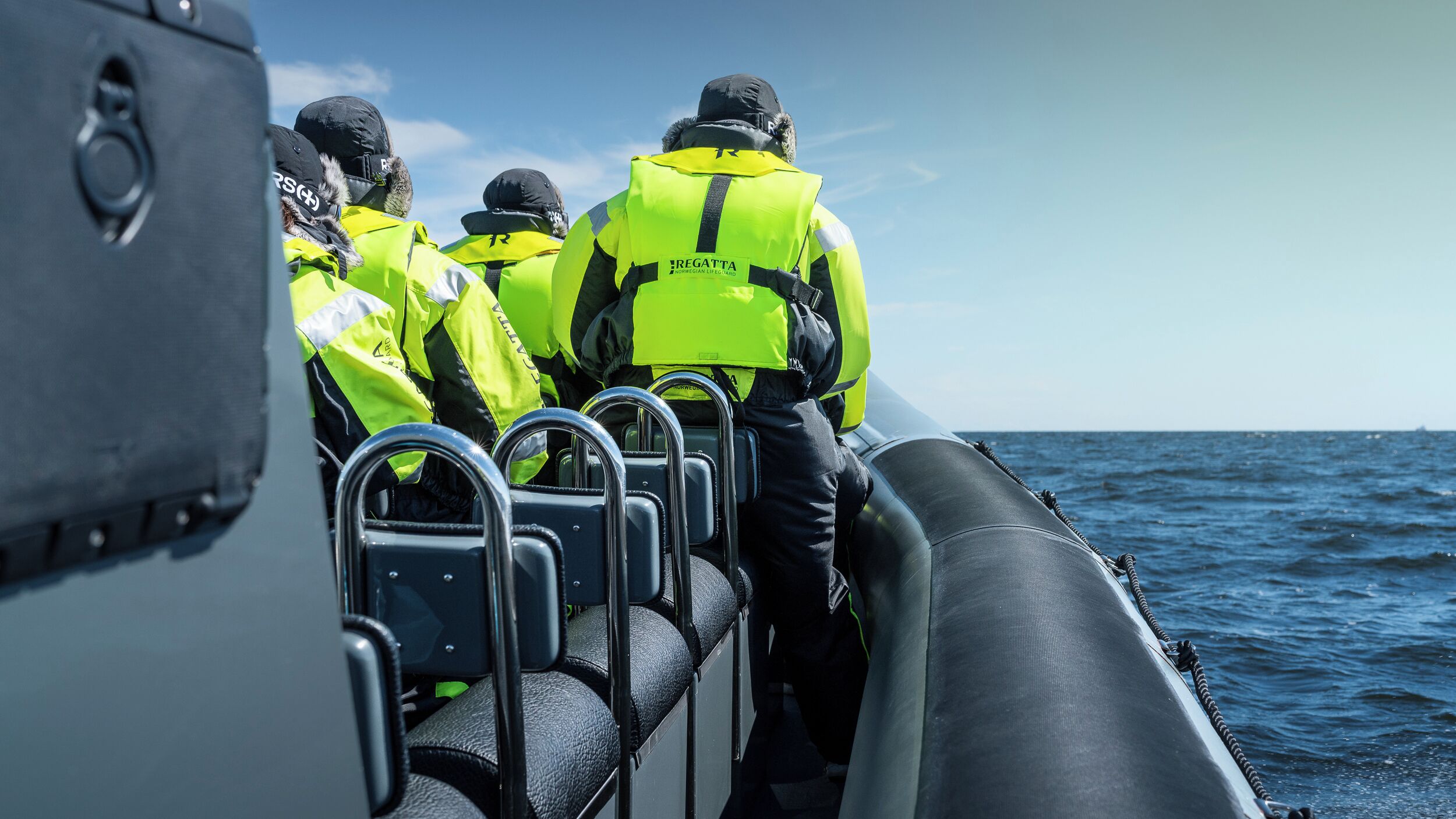 A group of people in high-visibility jackets on a boat, with metal railings and a view of the sea.