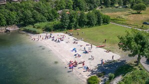 A beach with clear water, a sandy shore, and a grassy area with trees. - Havna Hotel & Sjøbad (Færder)