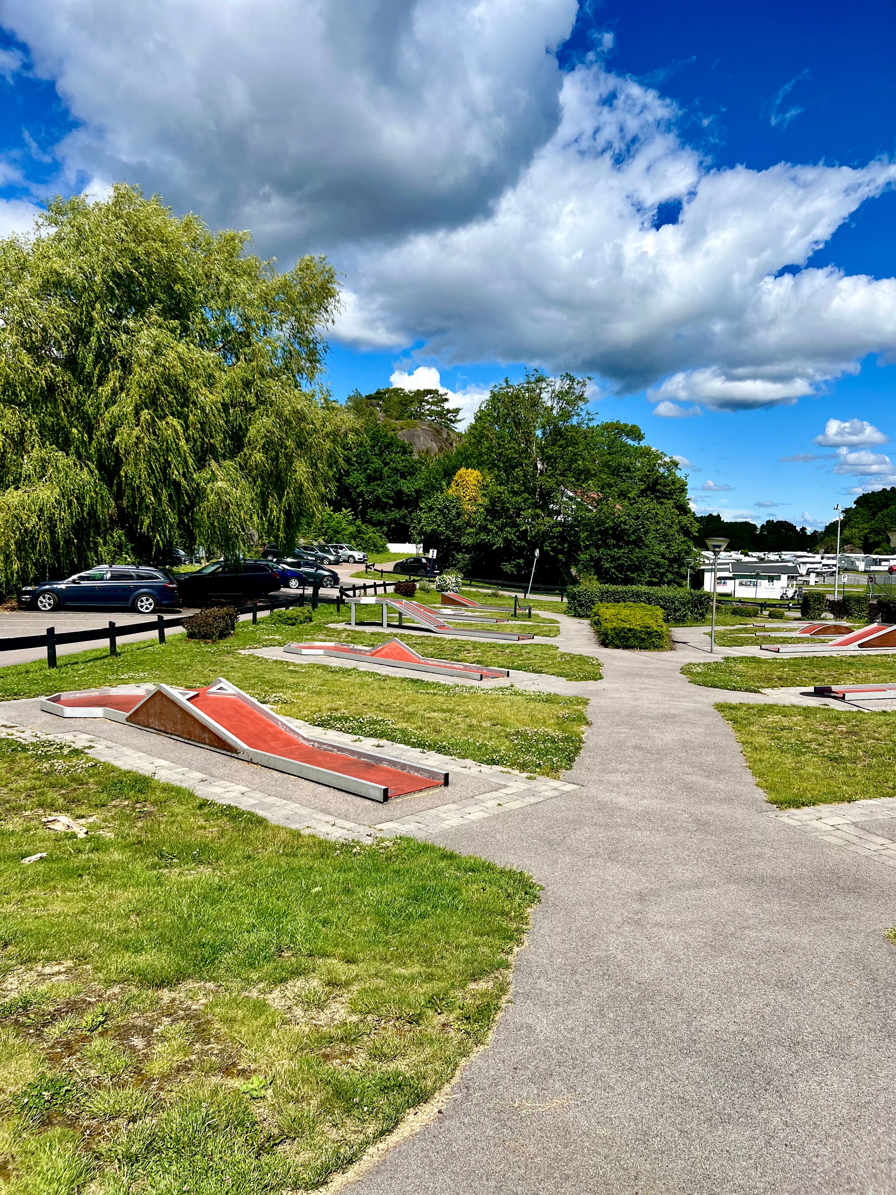 Un parque con un sendero pavimentado, césped verde y toboganes rojos.