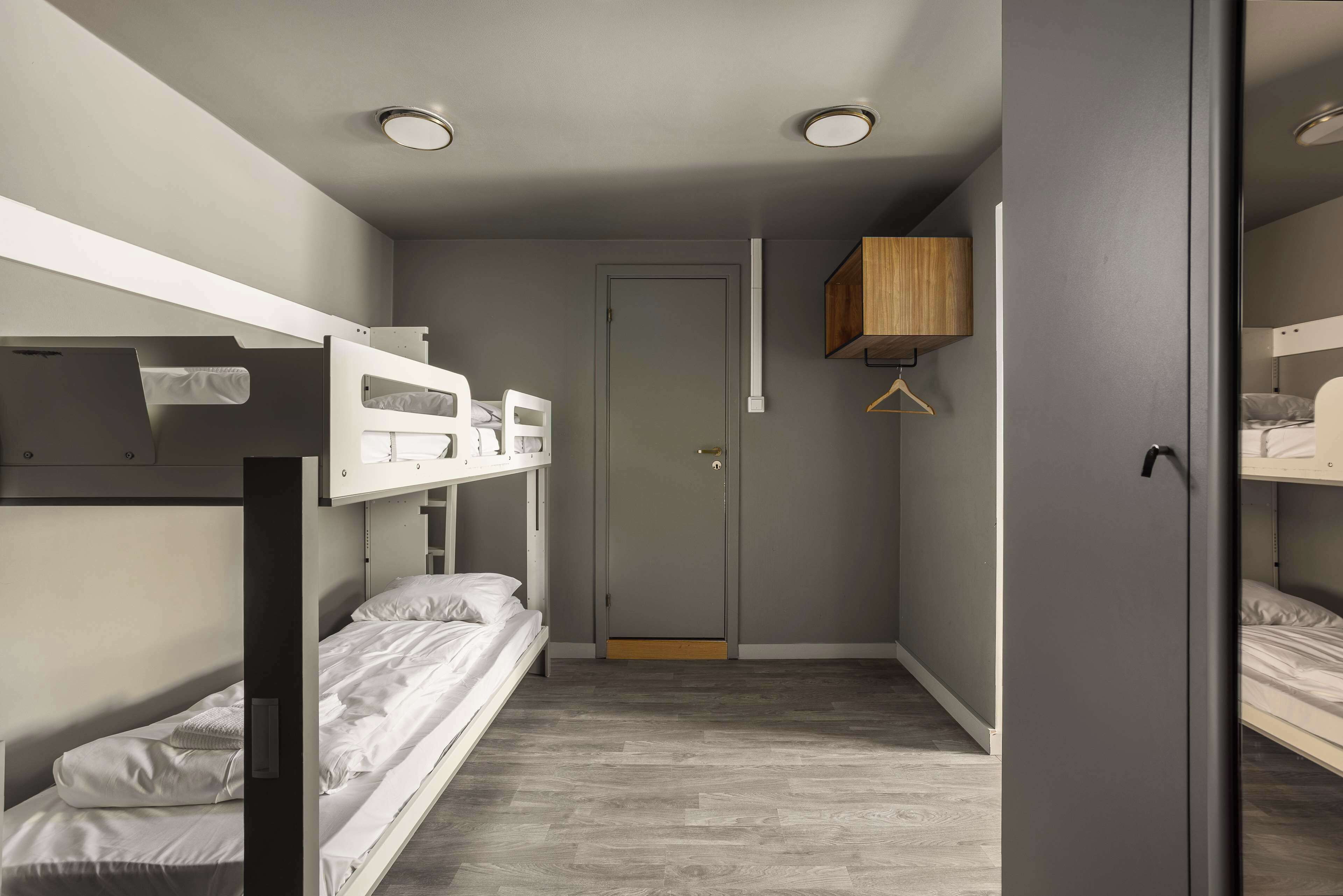 A narrow room with bunk beds, a door, and a wooden shelf.