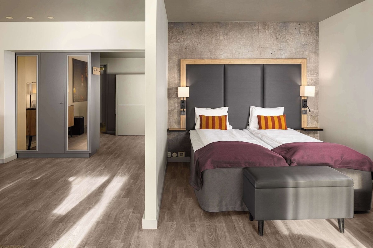 A modern bedroom with a large bed, bedside lamps, and a view into a bathroom.