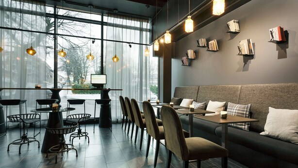A modern cafe with a large window, multiple tables, chairs, and a sofa. - Scandic Sarpsborg (Sarpsborg)