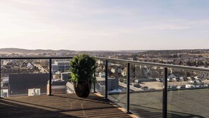 A balcony with a large potted plant, a view of a parking lot, and buildings in the distance. - Scandic Sarpsborg (Sarpsborg)