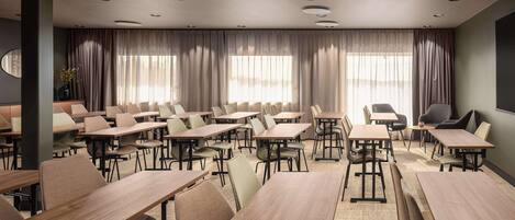 Une salle de conférence dotée de plusieurs tables et chaises, de grandes fenêtres avec des rideaux et d’un éclairage encastré au plafond.