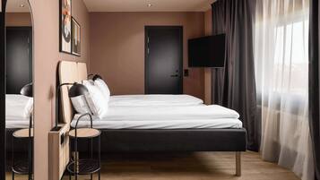 Ein modernes Hotelzimmer mit einem großen Bett, einem Flachbildfernseher, einem Spiegel und Blick ins Freie durch transparente Vorhänge.