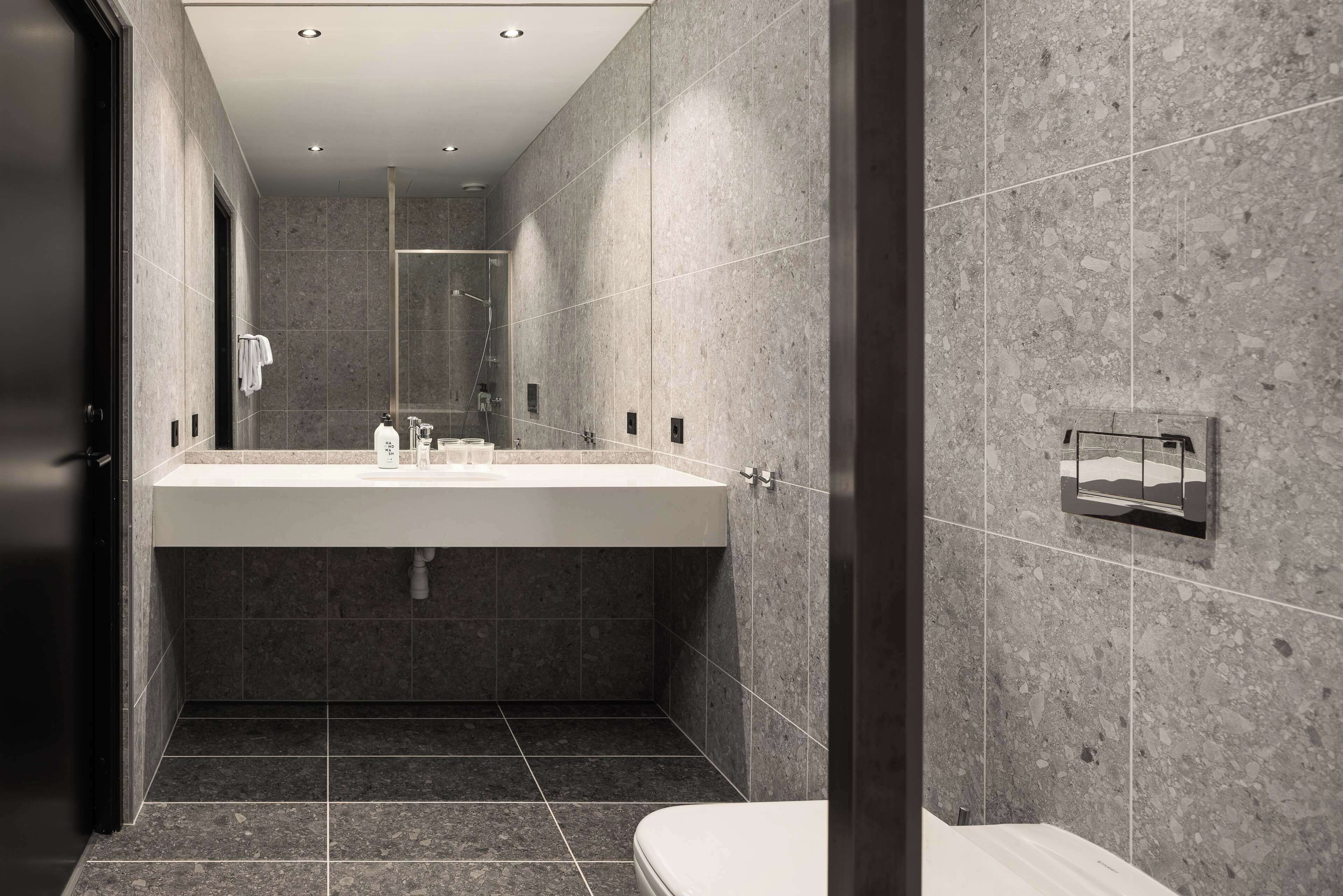 A modern bathroom with a large sink, dark tiles, and a glass shower enclosure.