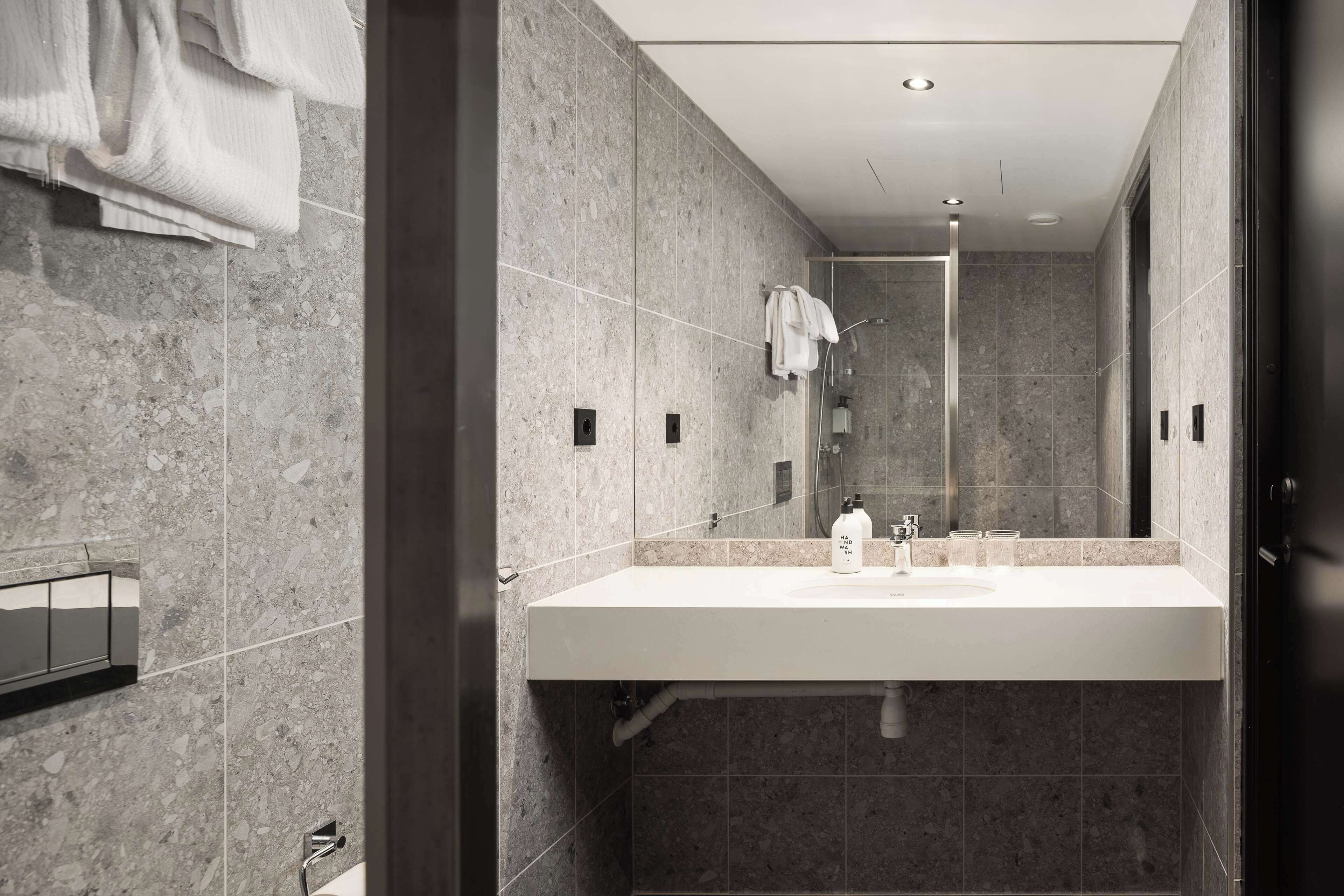 A modern bathroom with a large mirror, a white sink, and a shower area.