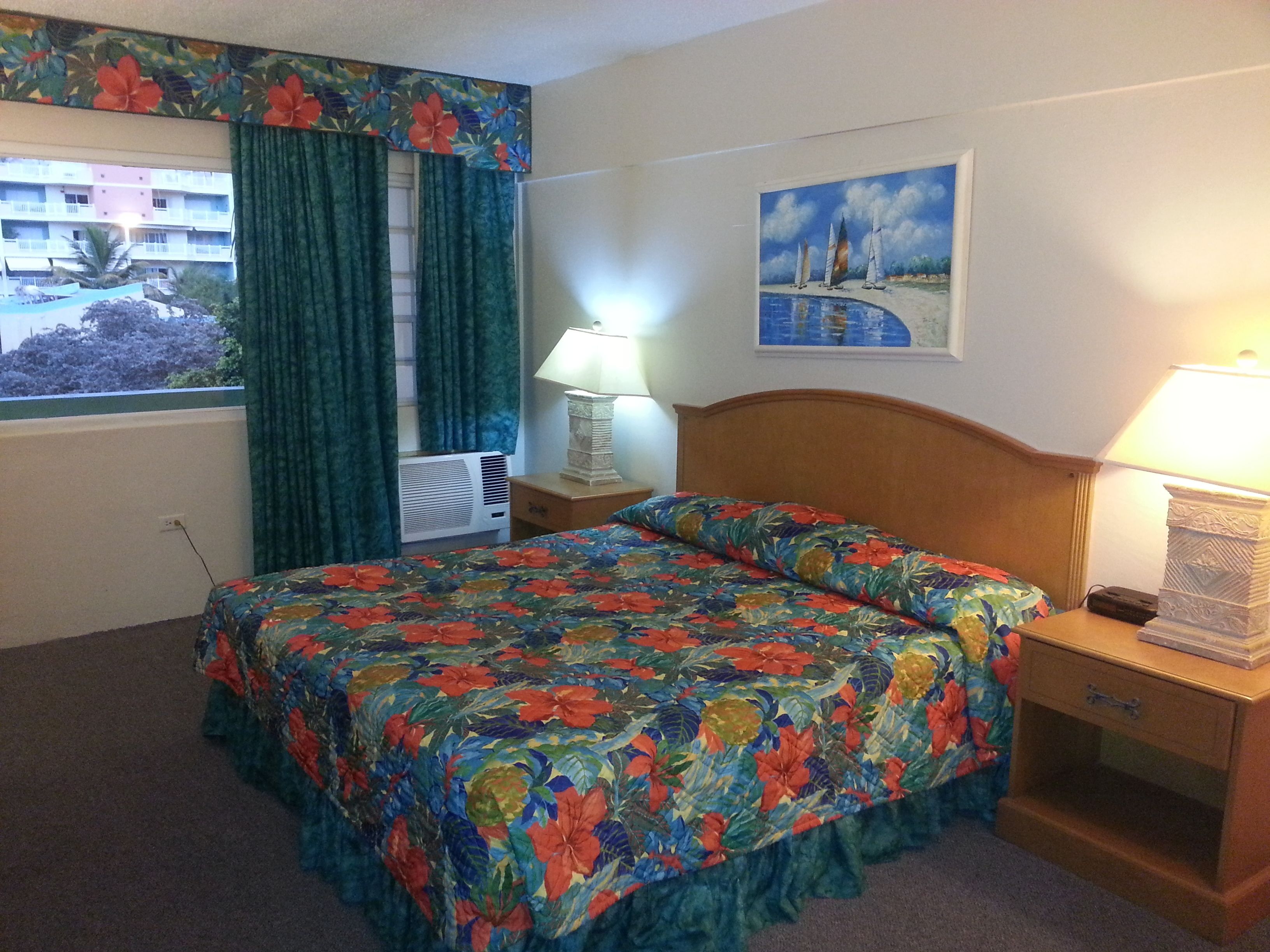 Una habitación de hotel con una cama, una mesita de noche, una lámpara, una ventana con cortinas y un cuadro en la pared.