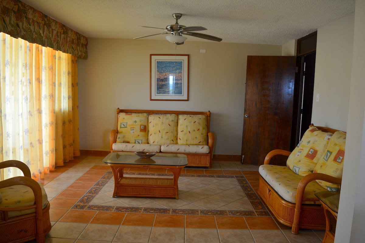 A living room with a sofa, chairs, a coffee table, and a ceiling fan.