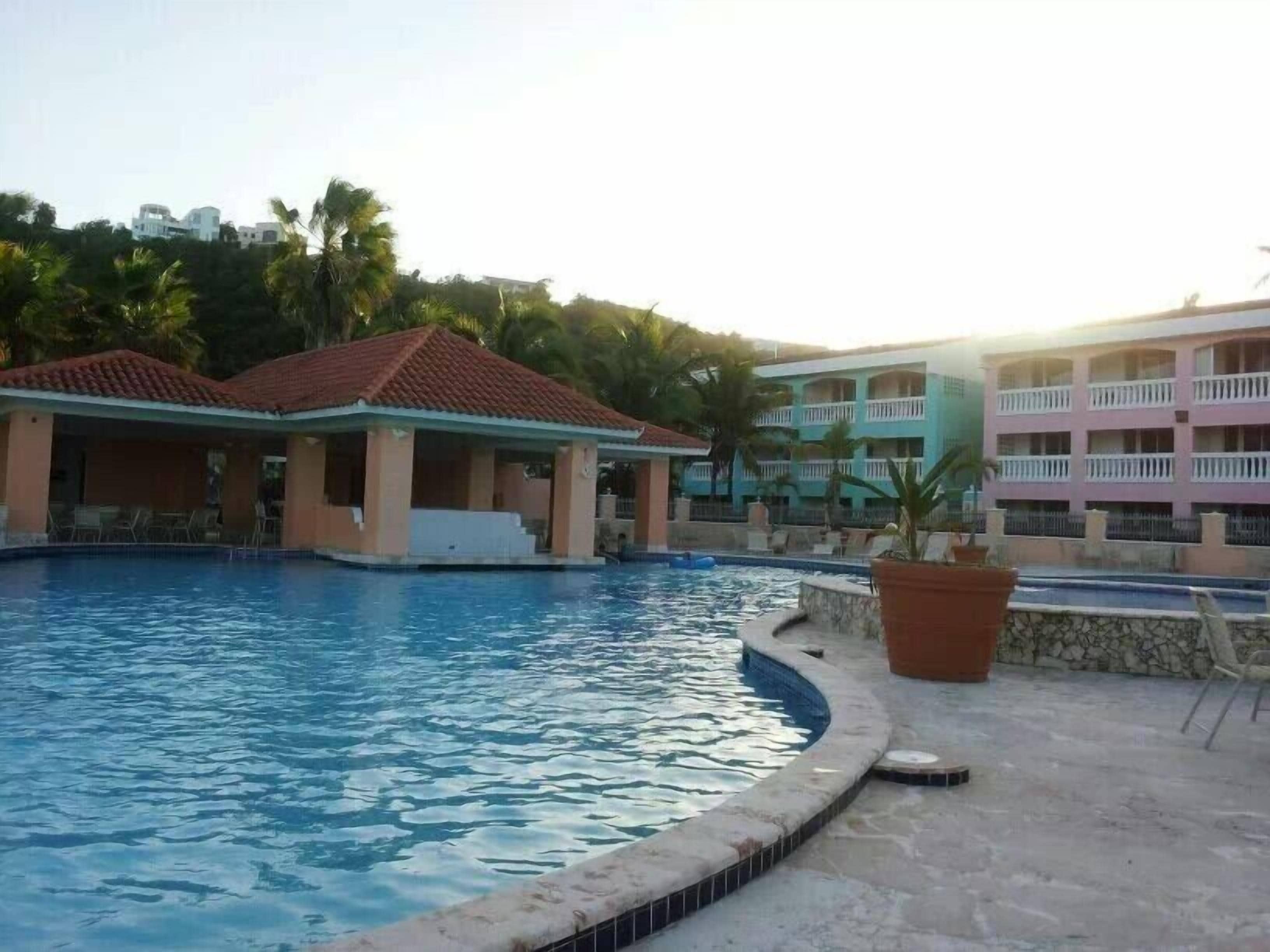 Una piscina con zona cubierta, terraza de baldosas de piedra y un edificio con balcones al fondo.