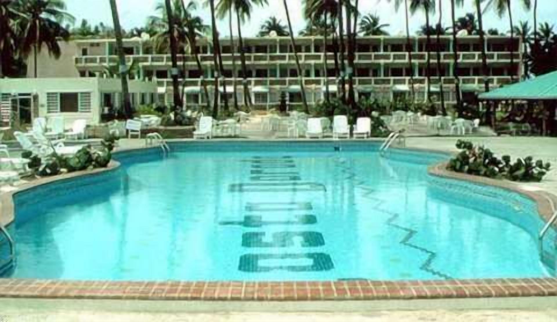 Une piscine entourée de chaises longues et de palmiers, le tout bordé par un bâtiment d’hôtel.
