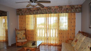 A living room with a ceiling fan, a glass-top coffee table, a wicker sofa, and a patterned armchair. - Villas de Costa Dorada Isabela (Isabela)