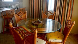 A dining area with a round glass table surrounded by wooden chairs, a woven placemat, and a patterned cushion. - Villas de Costa Dorada Isabela (Isabela)
