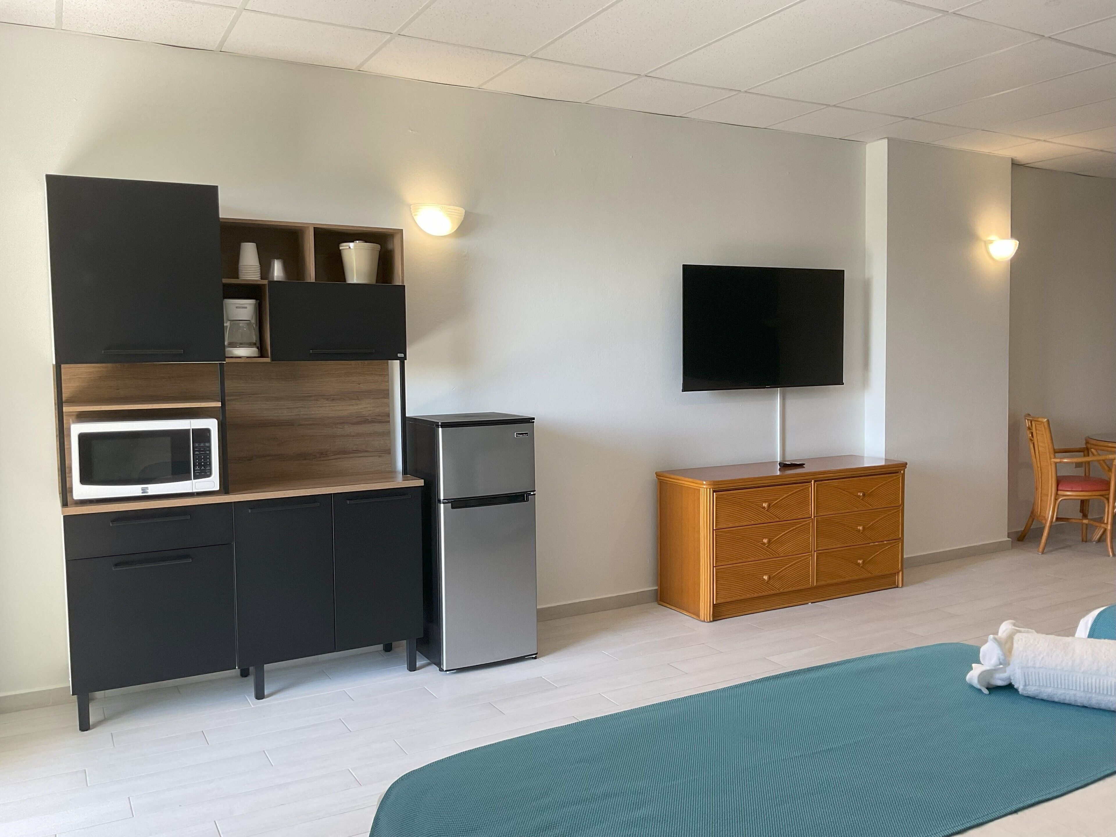 Une chambre moderne équipée d’un lit, d’une télévision, d’une kitchenette avec un four à micro-ondes et un réfrigérateur, ainsi que d’une armoire en bois.