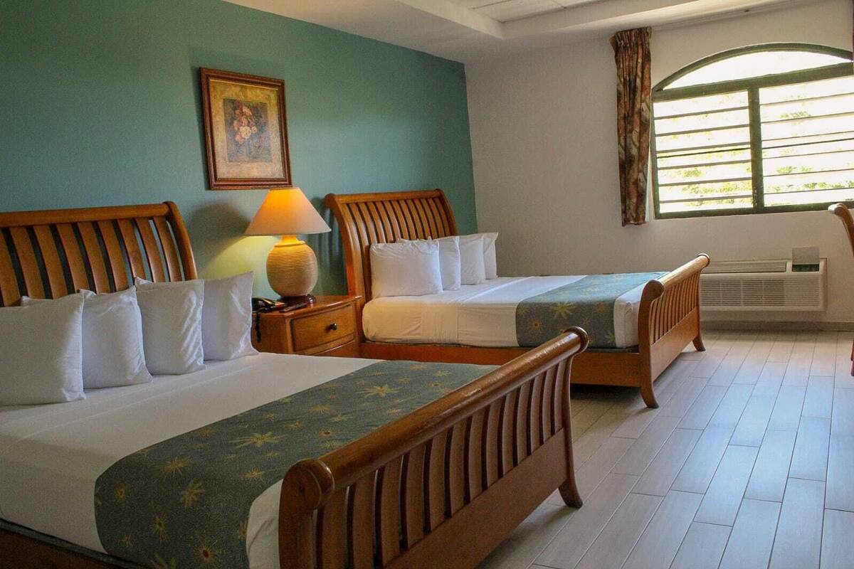 A hotel room with two wooden beds, a nightstand with a lamp, a framed picture on the wall, and a window with curtains.