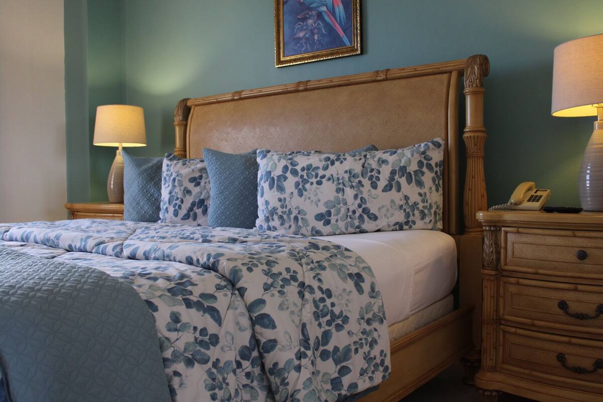 A neatly made bed with floral bedding, a wooden headboard, and a bedside table with a lamp.
