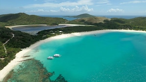 Un paysage côtier avec des eaux turquoise, une plage de sable et des bateaux ancrés près du rivage.