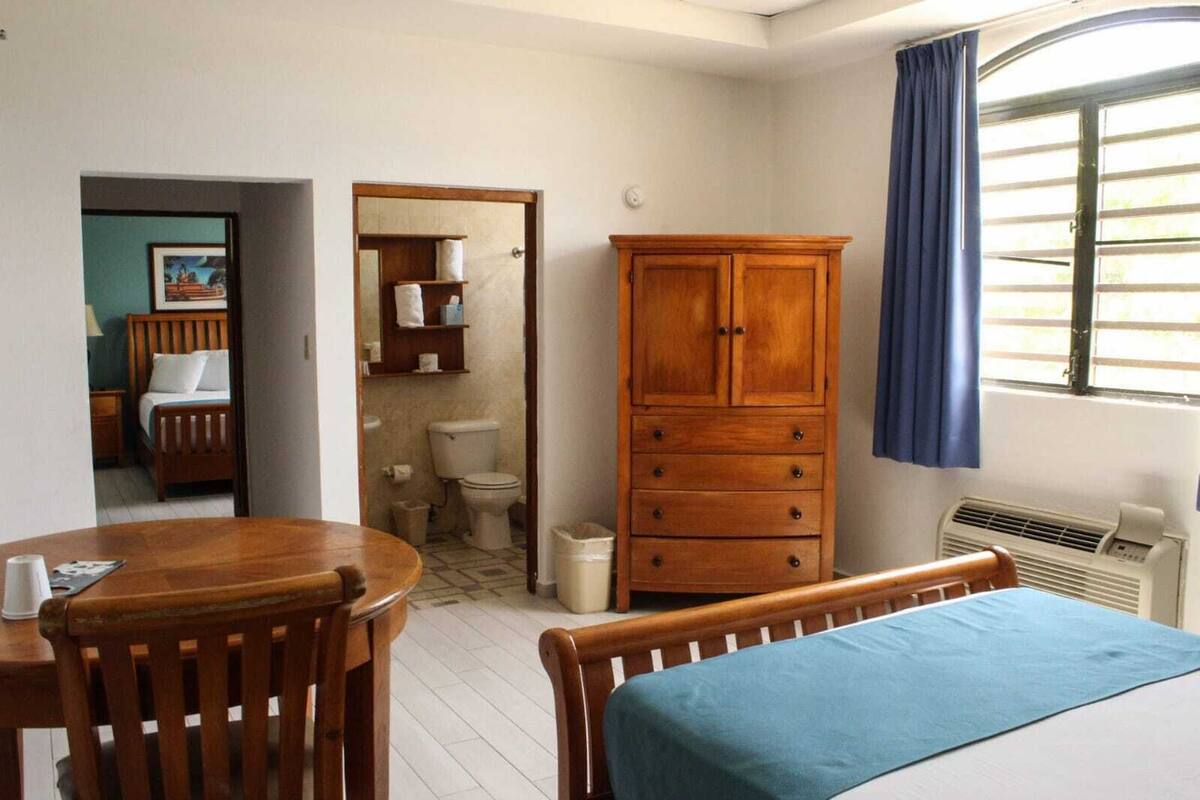 A room with a bed, a wooden cabinet, a small bathroom, and a window with curtains.