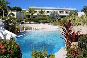 A swimming pool with a clear blue water, surrounded by tropical plants and a building in the background. - Fajardo Inn (Fajardo)