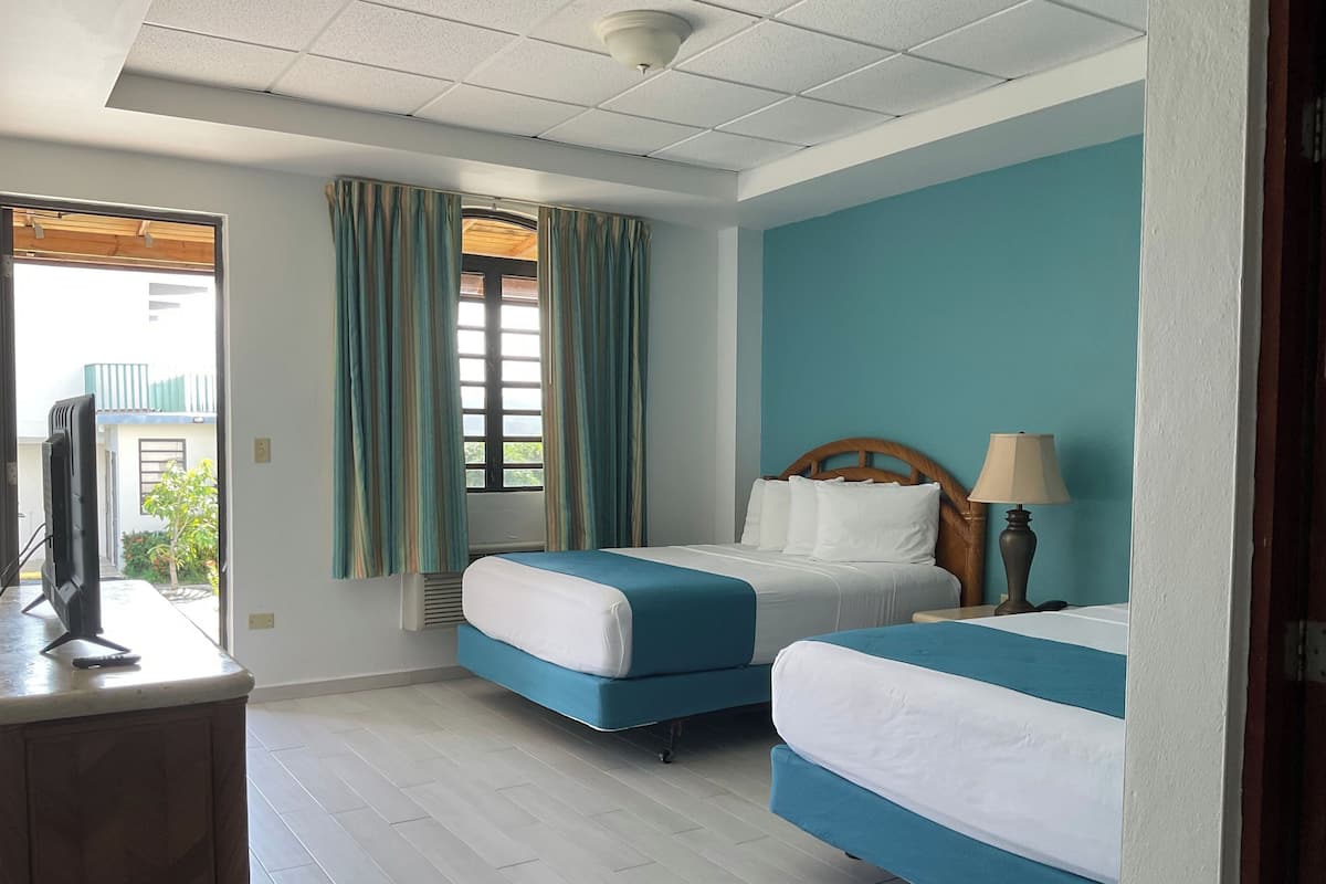 A hotel room with two beds, a TV, and a window with curtains.