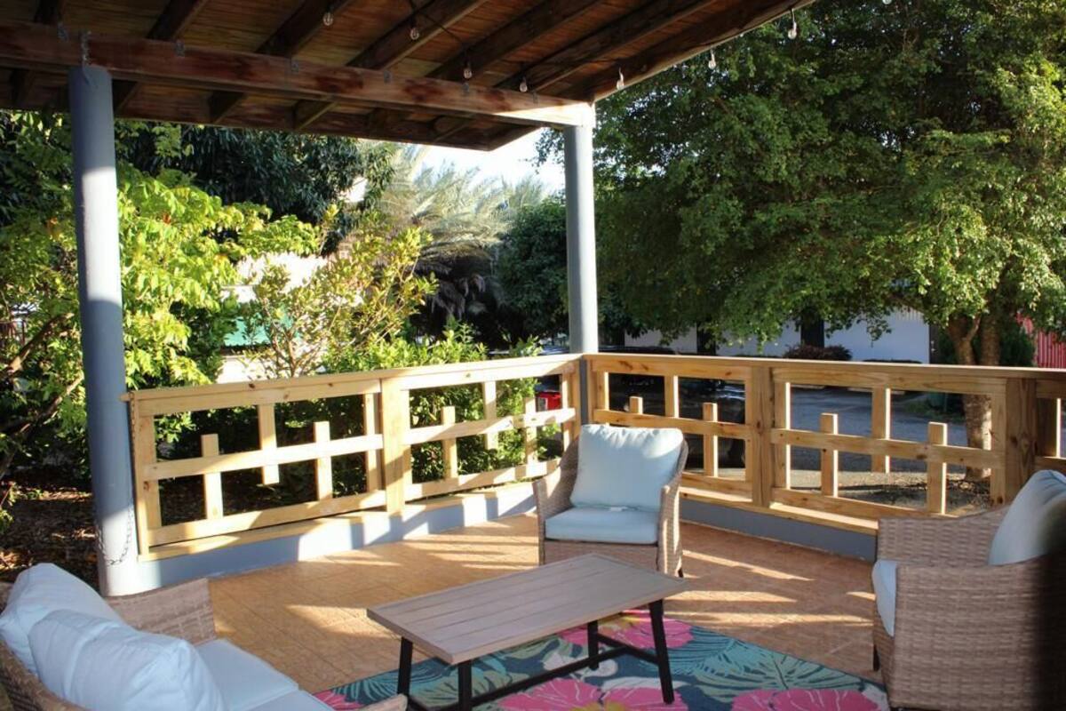 An outdoor patio with wooden furniture, a covered area, and a view of surrounding greenery.