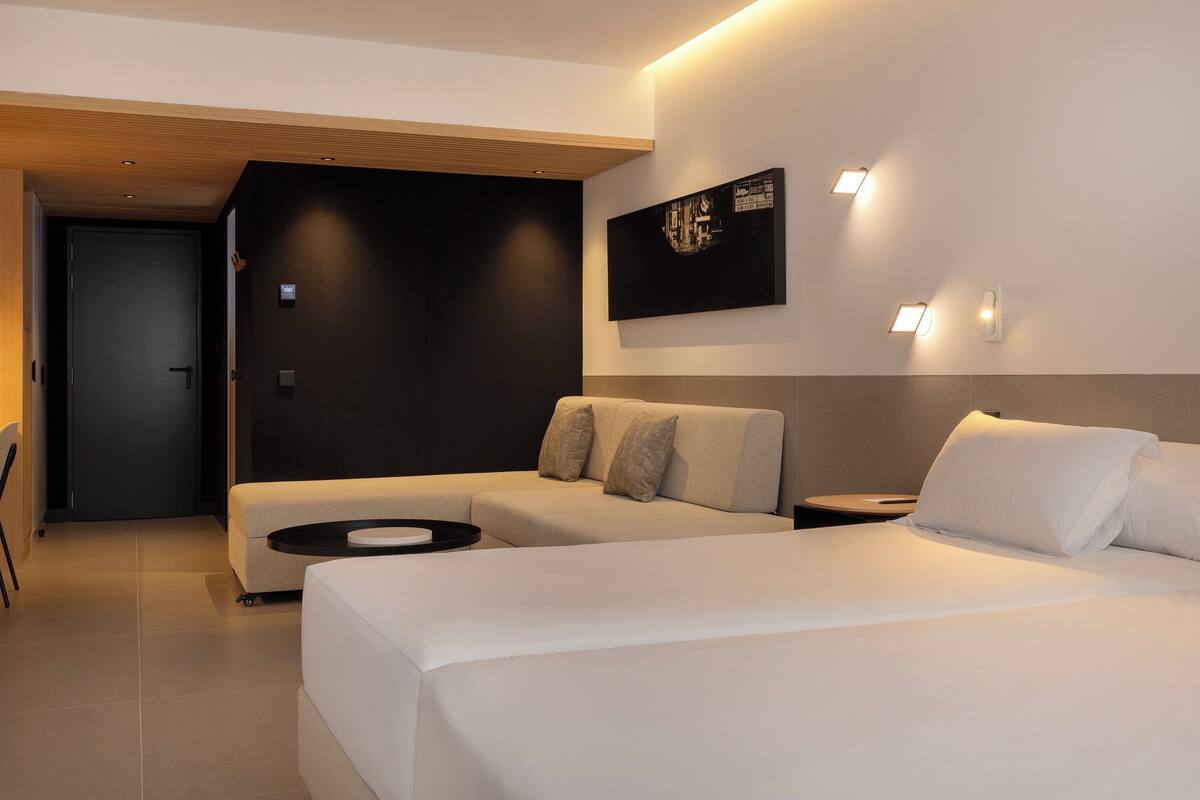 A modern hotel room with a large bed, a sofa, and a small table.