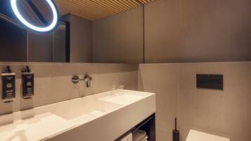 A modern bathroom with a large white sink, a mirror with a circular light, and a towel rack.