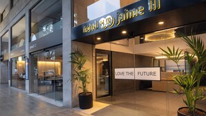 Moderne hotelentree met een glazen gevel, potplanten en een bord met de tekst 'LOVE THE FUTURE'.