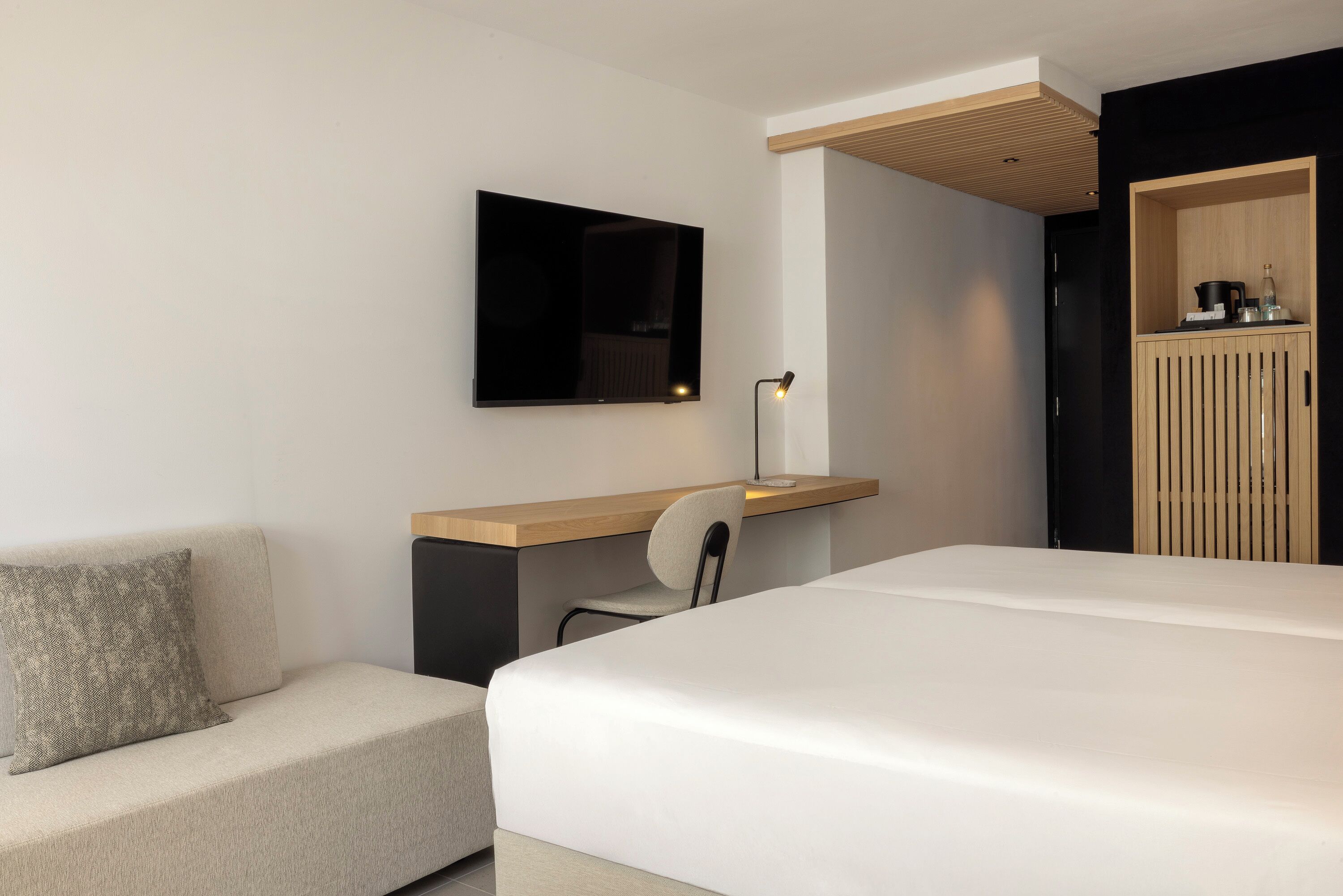 Una habitación de hotel moderna con cama, escritorio con silla, televisor de pantalla plana y armario.