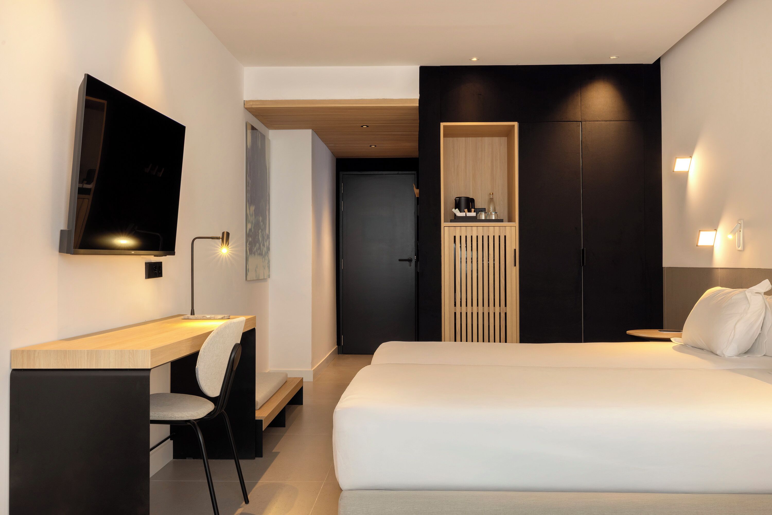 A modern hotel room with a bed, a desk, a chair, a TV, and a wardrobe.
