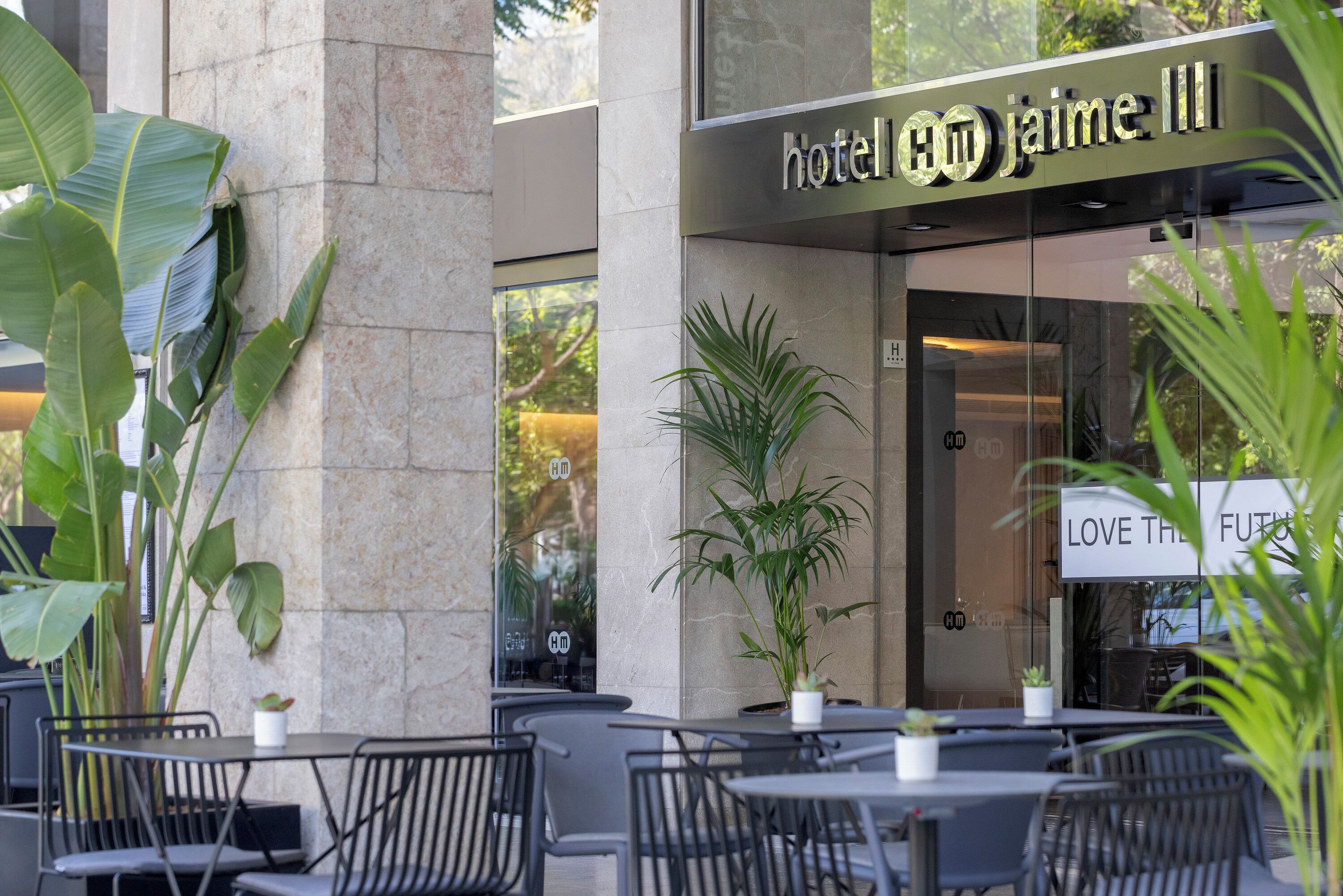 An outdoor seating area with tables and chairs, a large potted plant, and a hotel sign reading "hotel jaime III".