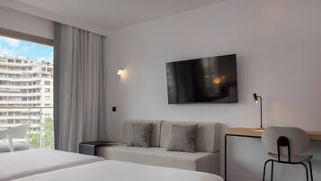 Habitación de hotel moderna con una cama grande, un sofá, un escritorio y una silla. Hay un televisor en la pared y una ventana con cortinas.