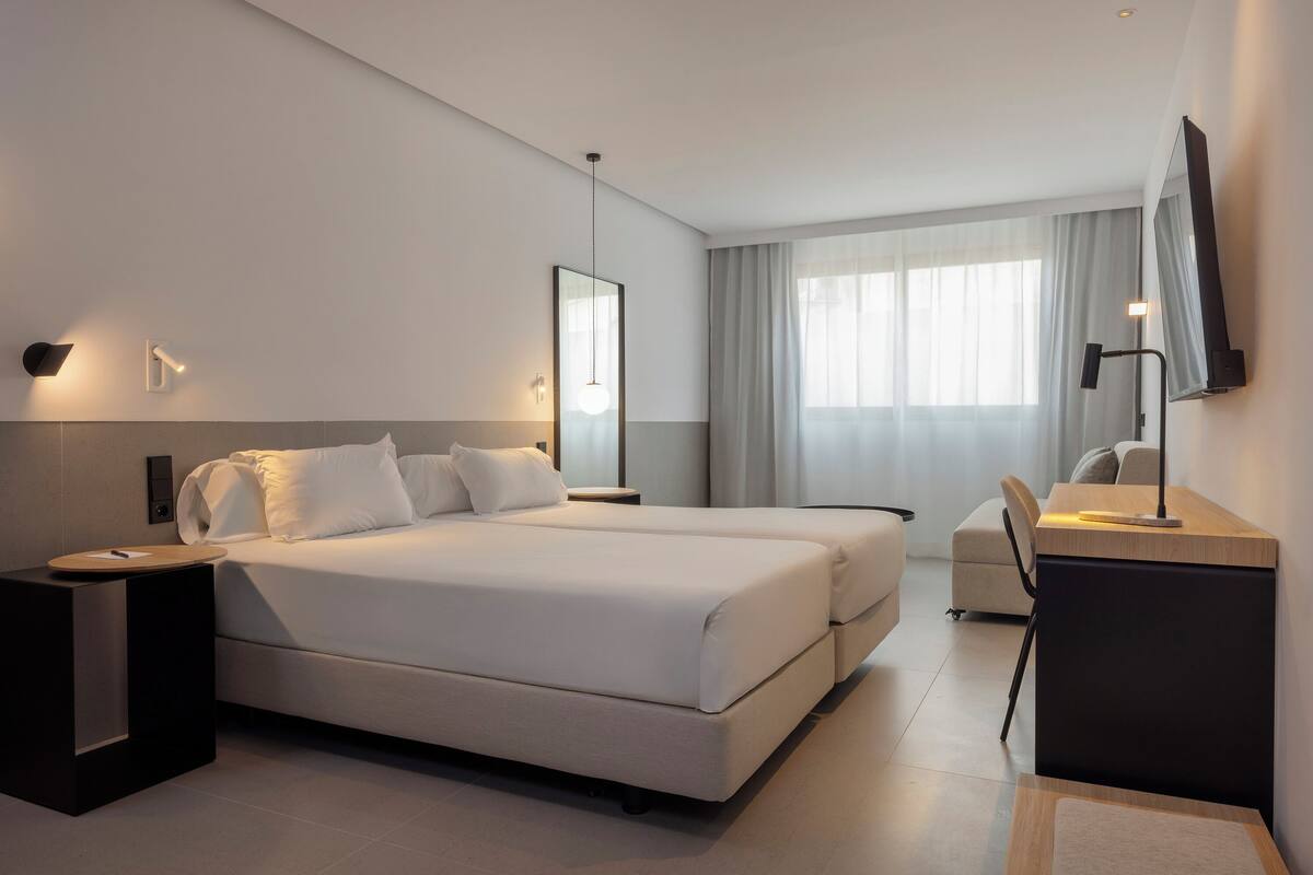 A modern hotel room with a large bed, bedside tables, a desk, and a TV.