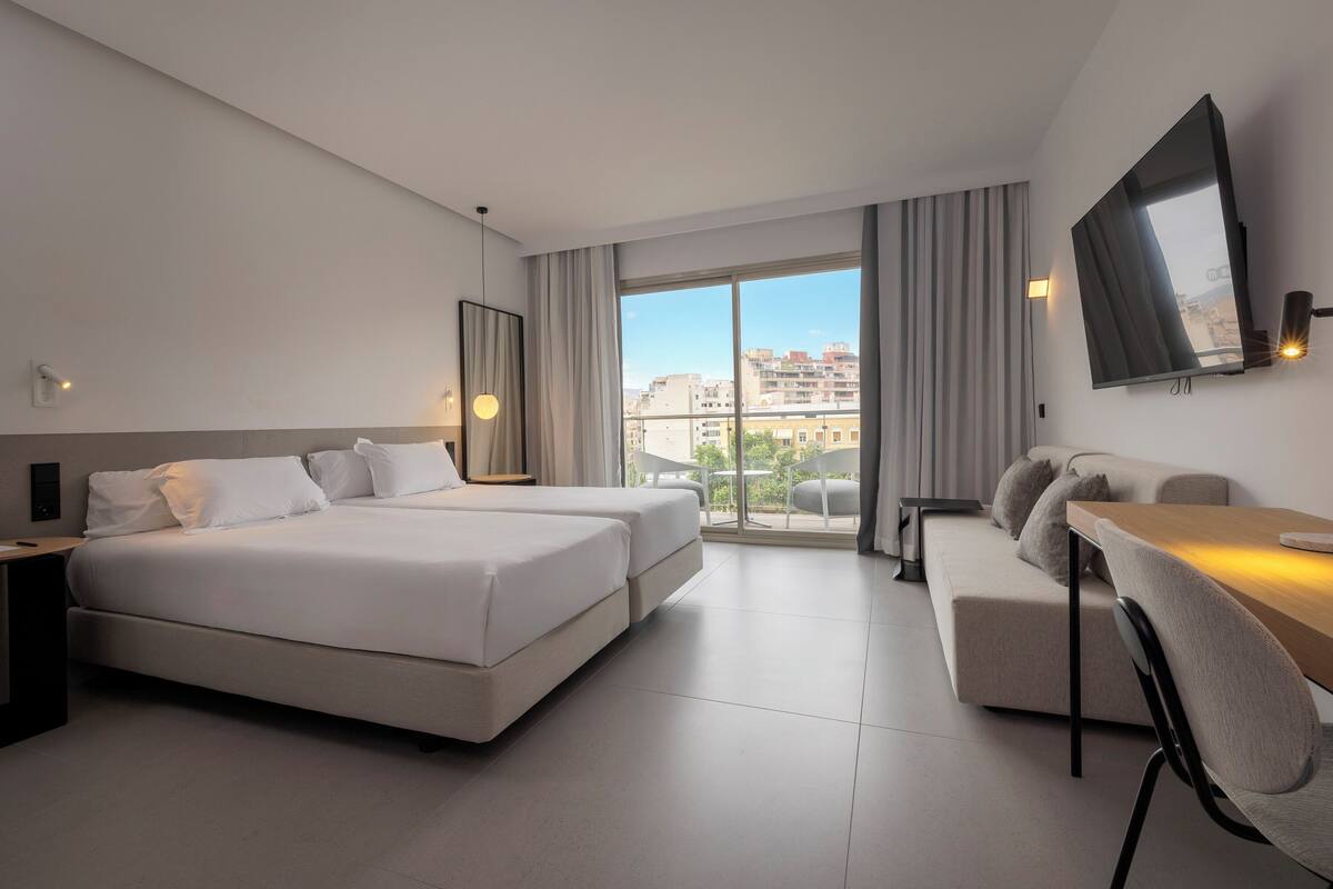 A modern hotel room with a large bed, a sofa, a desk, and a TV.
