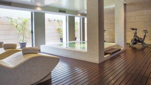 Een moderne spa-ruimte met houten vloer, een massagestoel, een jacuzzi en trainingsfietsen.