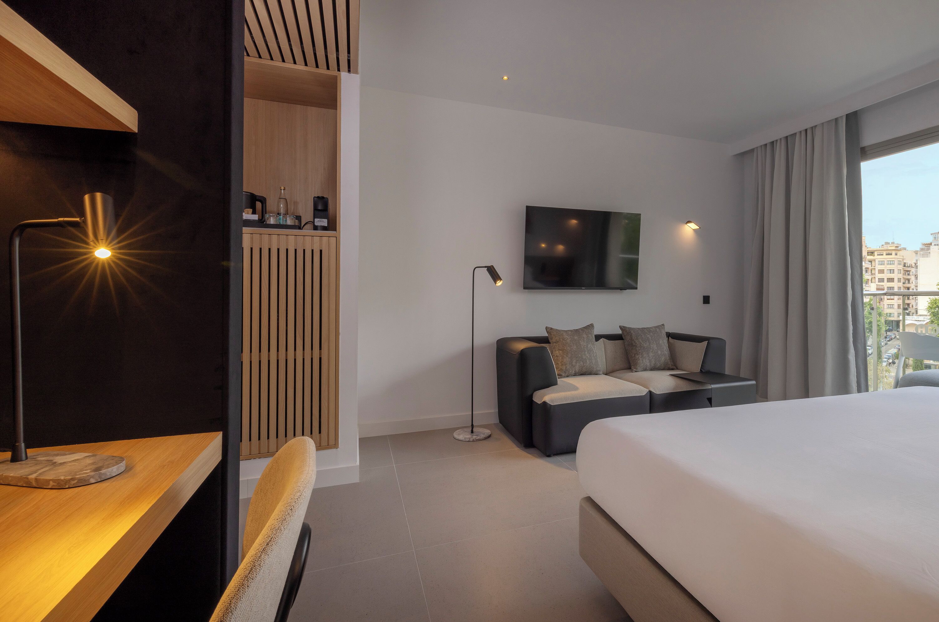 Una habitación de hotel moderna con una cama grande, un escritorio, televisión y vistas a la ciudad.