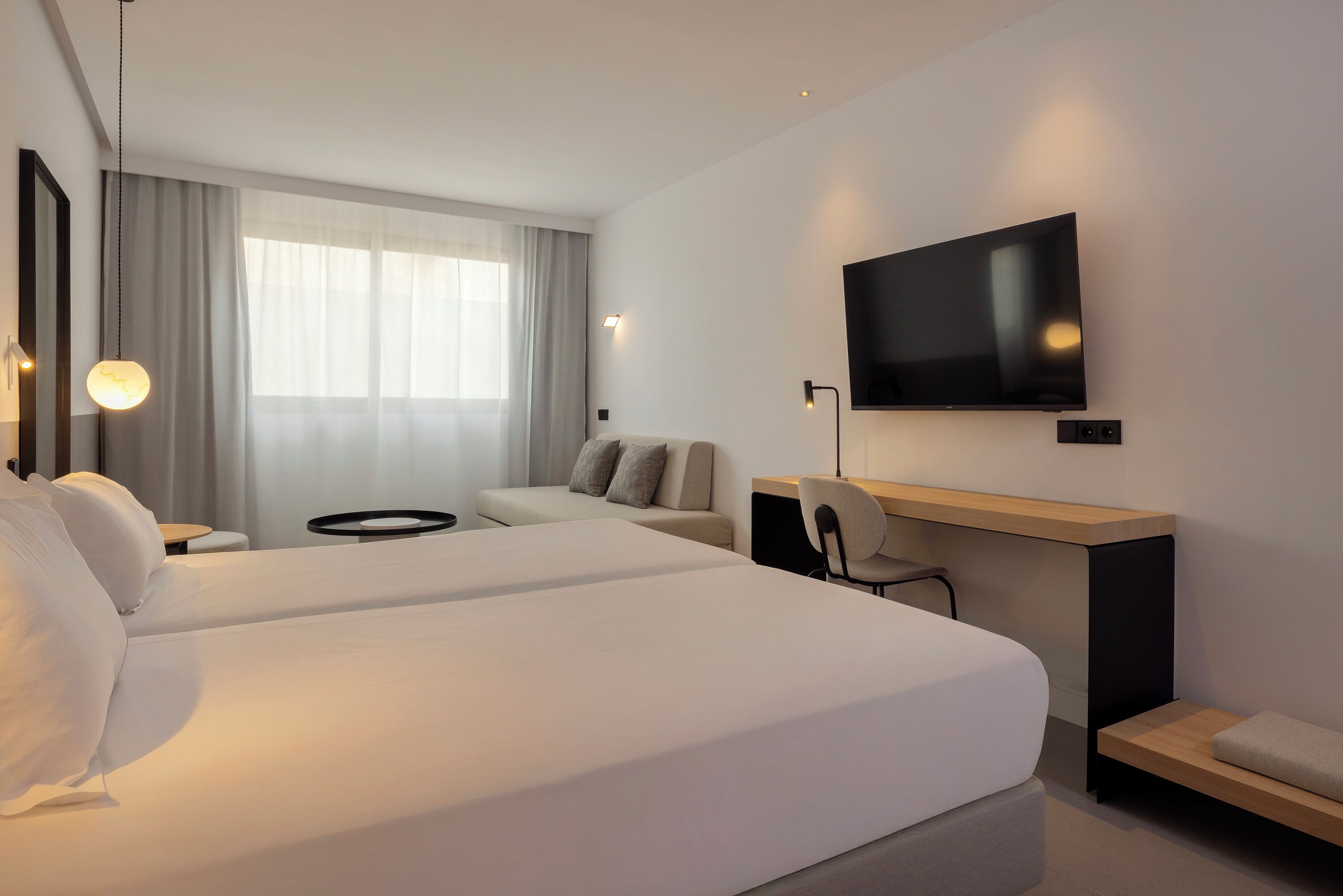 Una habitación de hotel moderna con dos camas, un escritorio, un televisor y un ventanal con cortinas.