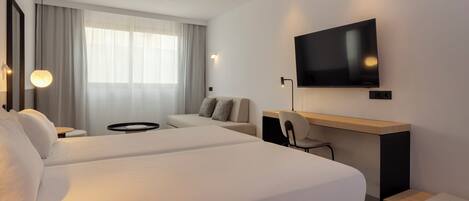 Una habitación de hotel moderna con dos camas, un escritorio, un televisor y un ventanal con cortinas.