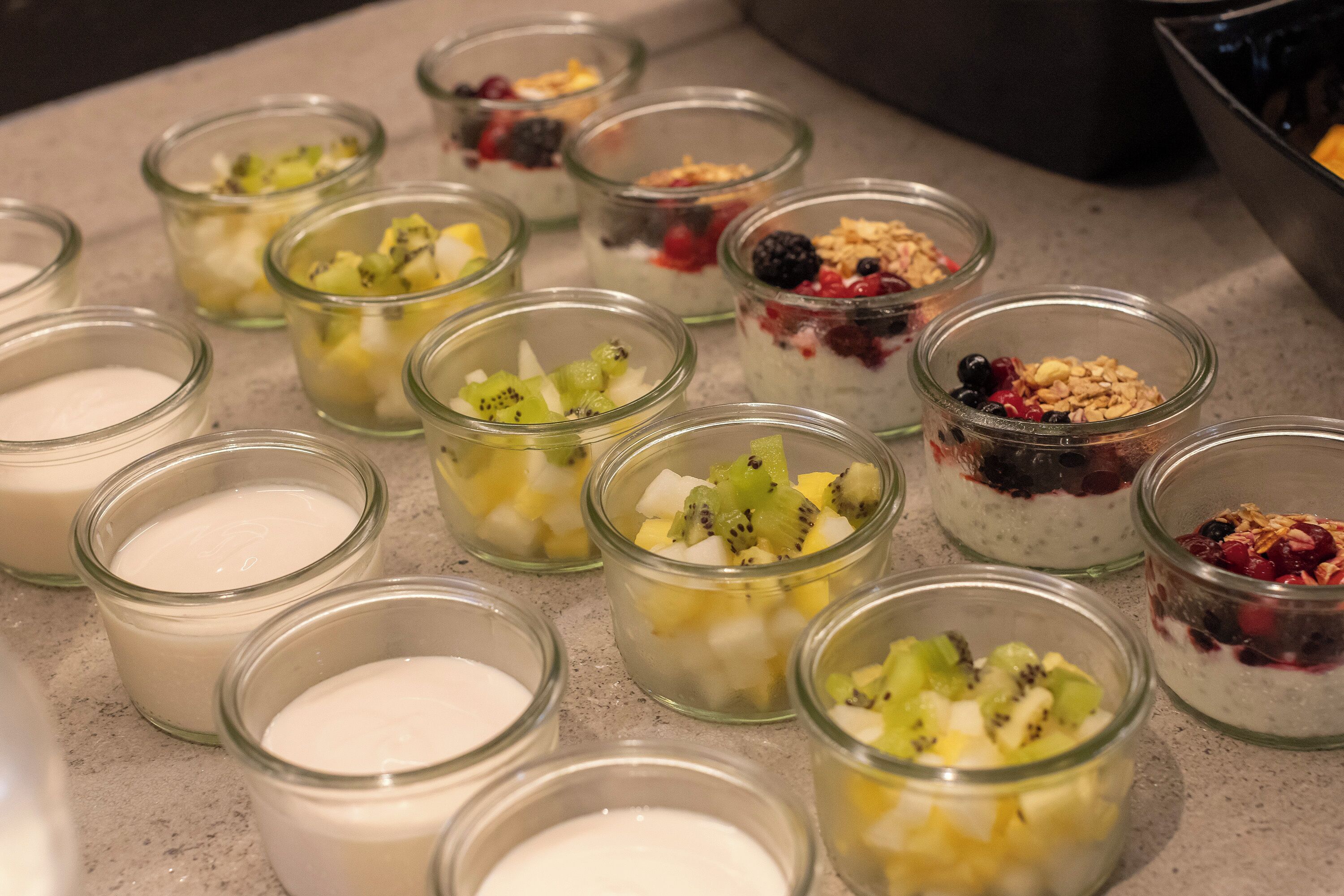 A variety of small glass bowls containing different types of yogurt topped with fruits and granola.