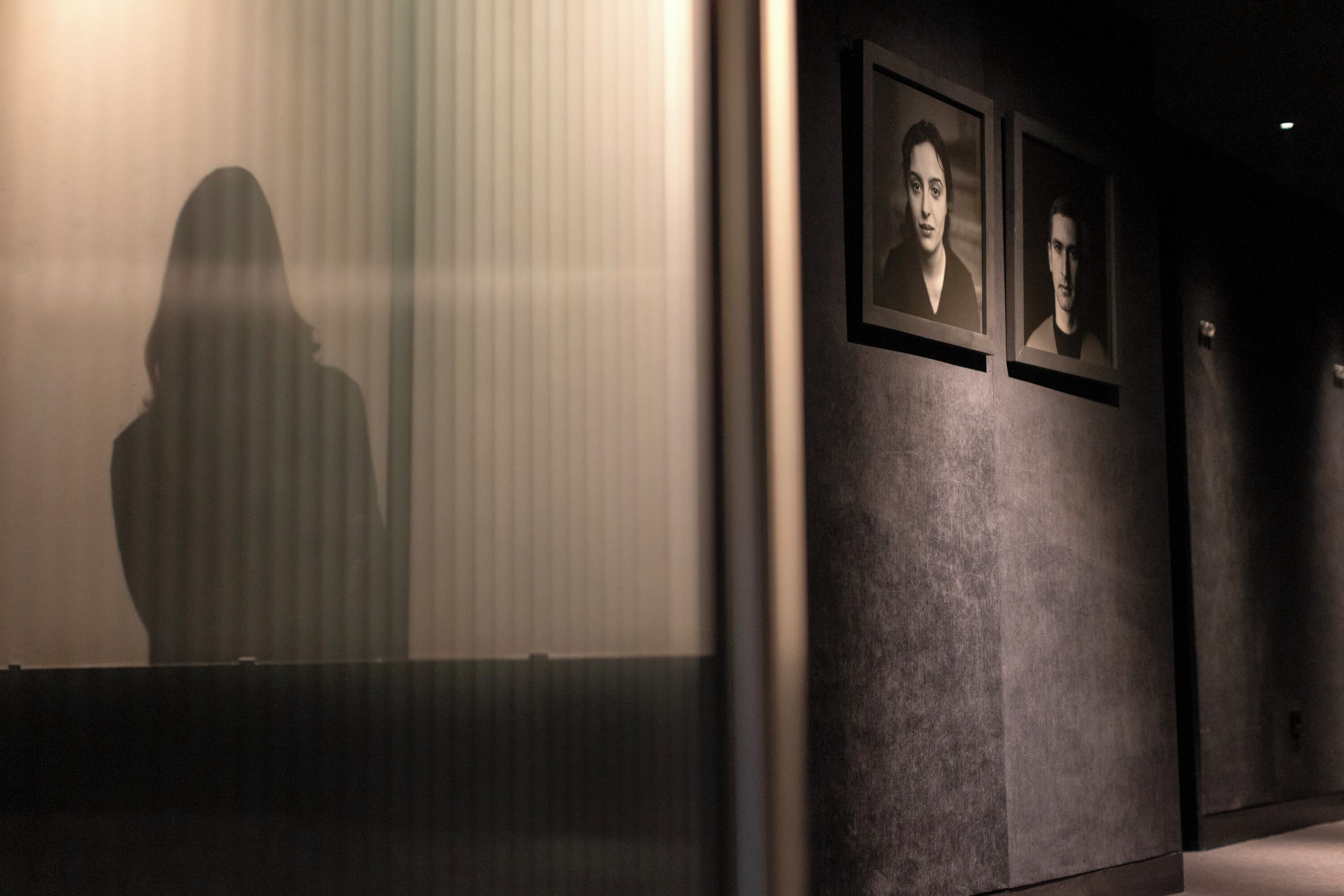 Un pasillo con retratos enmarcados en la pared, una superficie reflectante y la sombra de una persona.