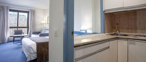 A hotel room with a bed, a desk, a chair, a window with curtains, a sink, and a mirror.