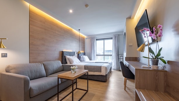 A modern hotel room with a bed, a sofa, a desk, and a TV.