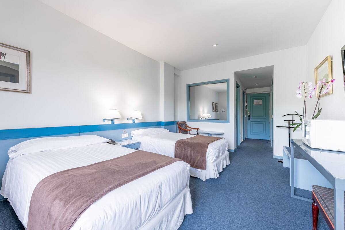 A hotel room with two beds, a desk, a chair, and a mirror.