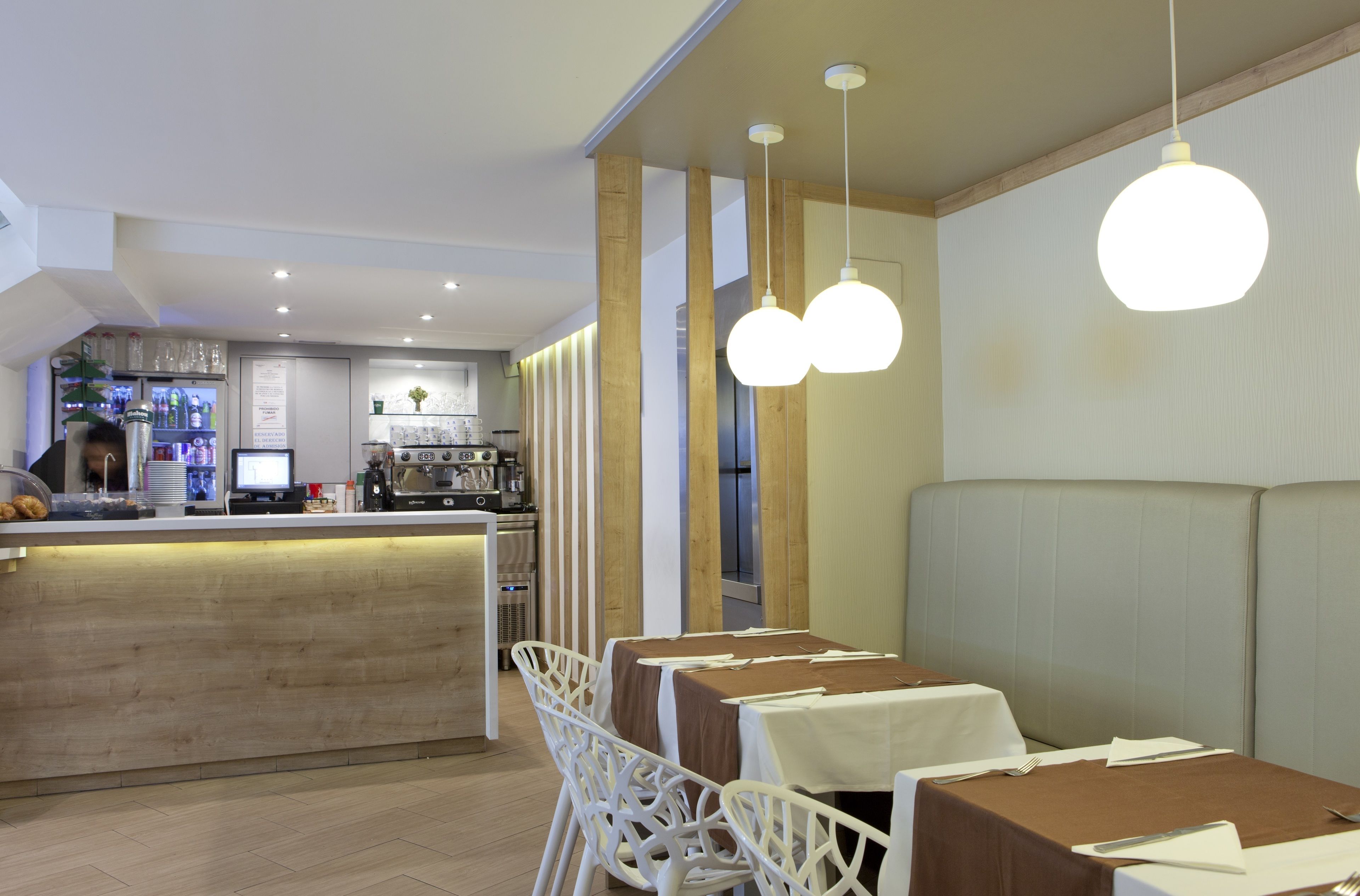 Restaurante com área de bar, cadeiras brancas e mesas com toalhas castanhas.