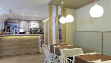 Restaurante com área de bar, cadeiras brancas e mesas com toalhas castanhas.