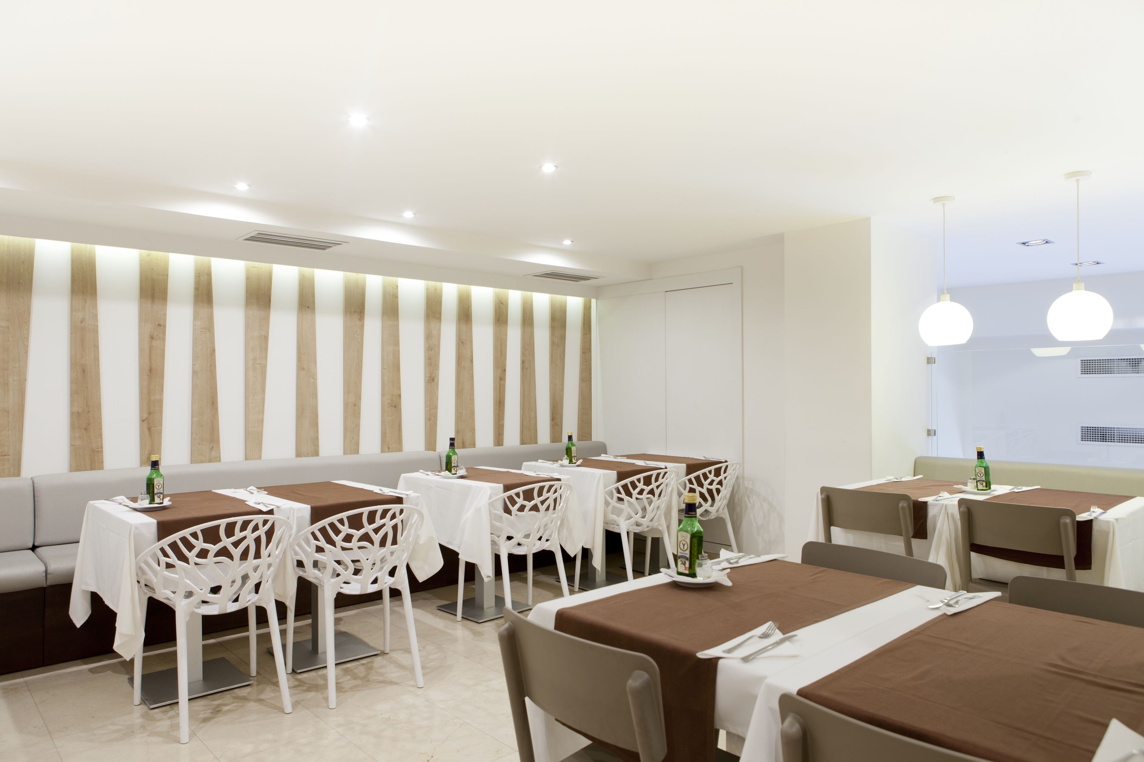 Een moderne eethoek met witte stoelen en tafels, een bank en een gestreepte wand.