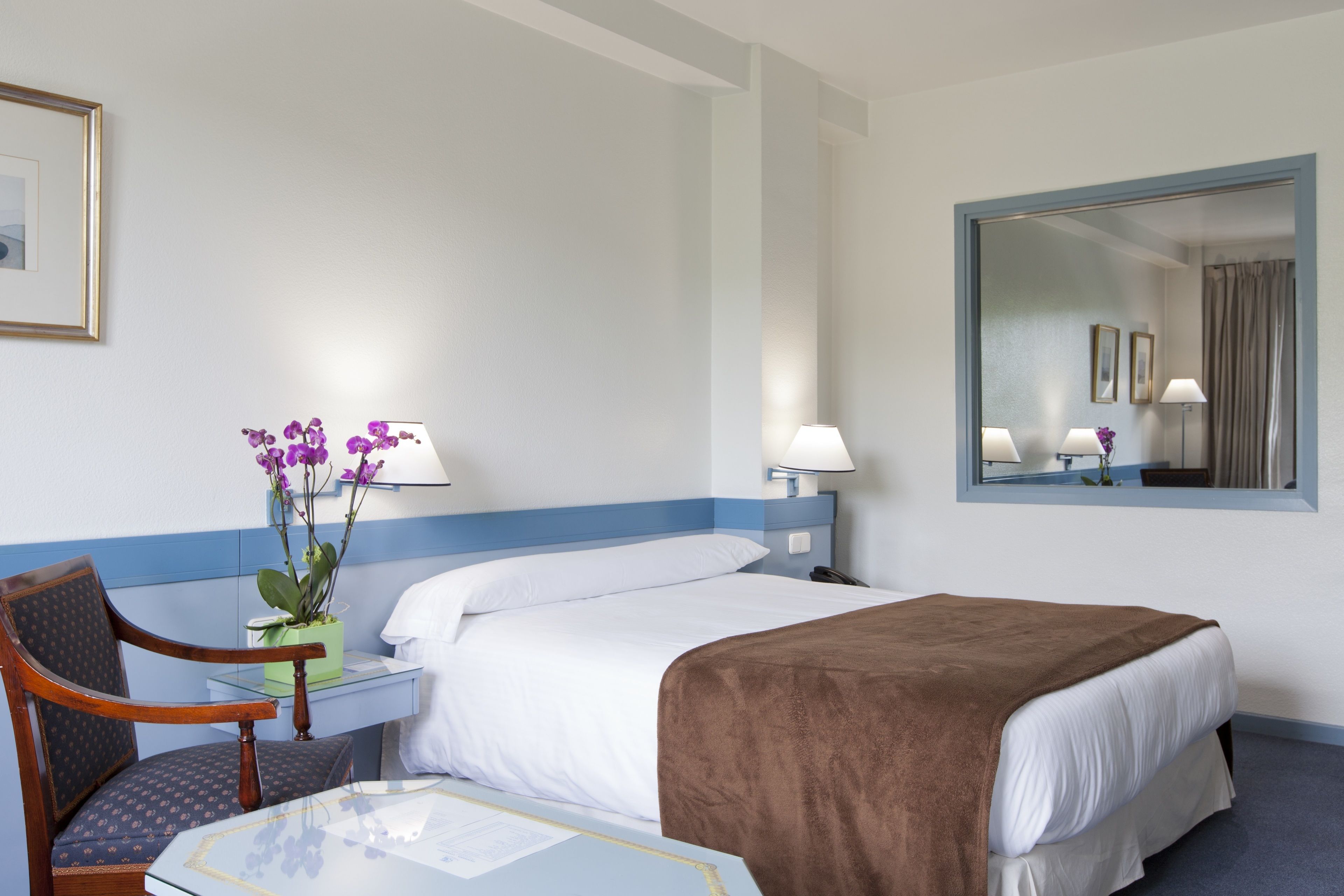 A hotel room with a bed, a chair, a desk, and a mirror.